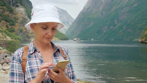 Una-Mujer-Usa-Un-Teléfono-Inteligente-En-La-Costa-De-Un-Pintoresco-Fiordo-En-Noruega,-Siempre-En-Tecnología-Táctil-O