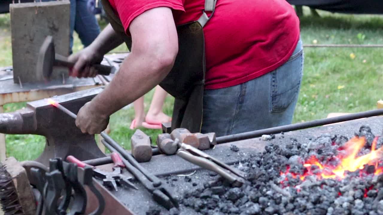Blacksmith hammering hot iron in slow motion with burning coals in foreground