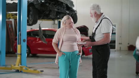 un viejo mecánico de automóviles tomando datos sobre el coche y firmando y estrechando la mano de una mujer adulta en el servicio de automóviles.