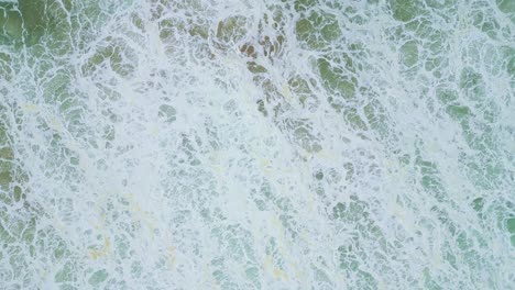 foamy waves crash on a shore in aljezur, portugal, top-down aerial view