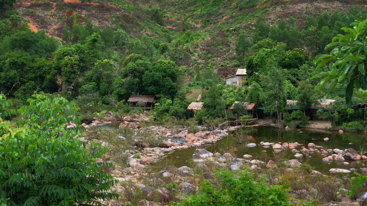 selva vietnamita con río, grandes rocas del río, y casas de chozas tradicionales por la orilla del río