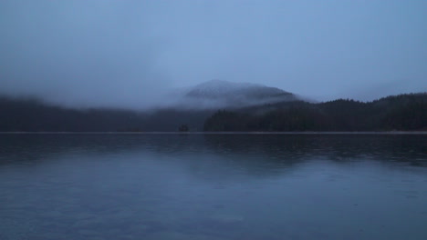 zugspitze mountain reflection in calm lake eibsee with low clouds across daybreak landscape