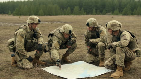 four soldiers in camouflage uniforms planning with a map in a field