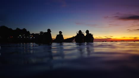 silhouettes of divers in ocean at sunset