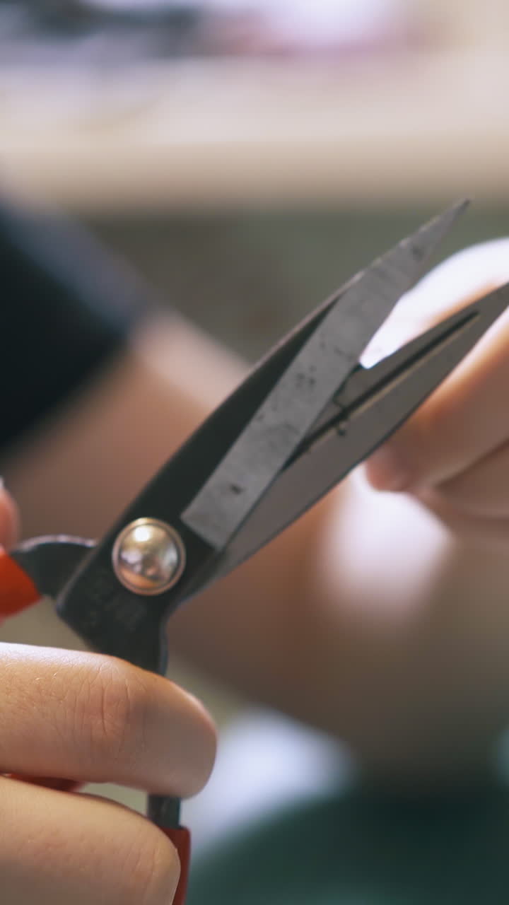 CU: Skilled girl designer cuts black leather strip edges with large red scissors in workshop extreme close view