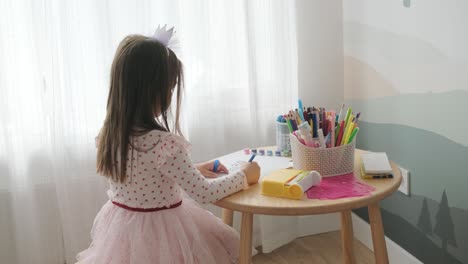 young girl sitting at a table, drawing with colorful crayons. ideal for themes of creativity, childhood development, learning, and art activities in a cozy indoor setting.