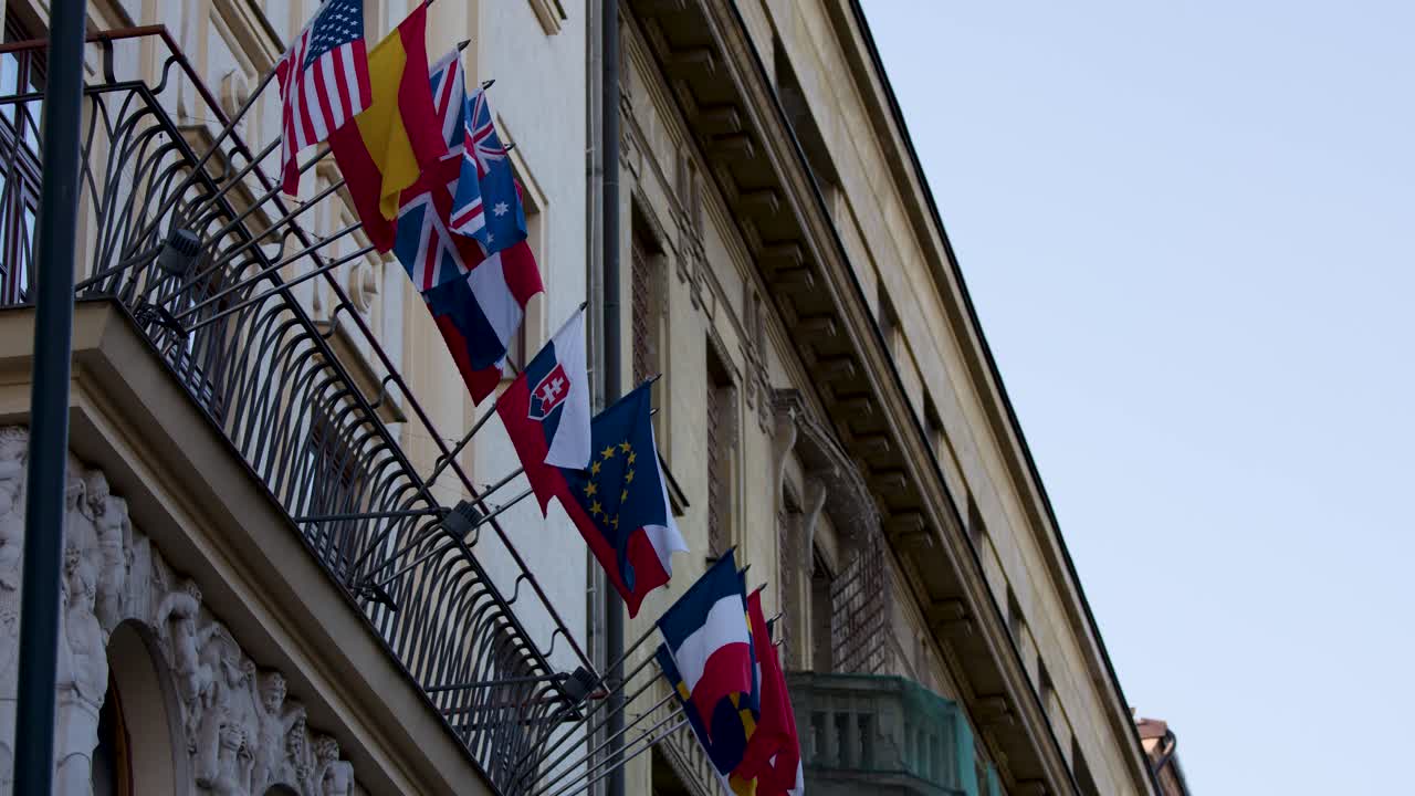 Multiple national flags wave on embassy building facade in Prague, daylight, slight upward camera movement