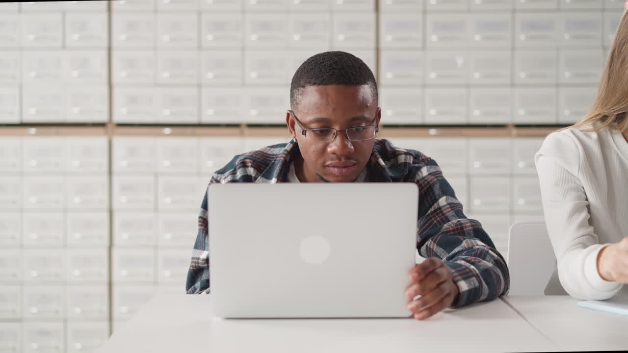 Black man works on laptop in library. African American student studies online information on computer in public library hall. E-learning advantages