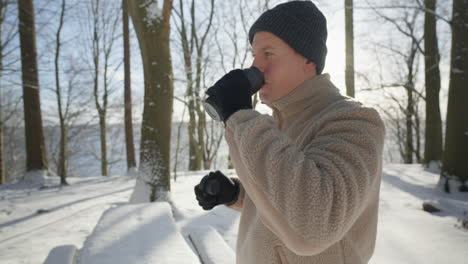 Person-enjoys-a-hot-drink-outdoors,-winter-sun-casting-a-warm-glow-on-a-frosty-day