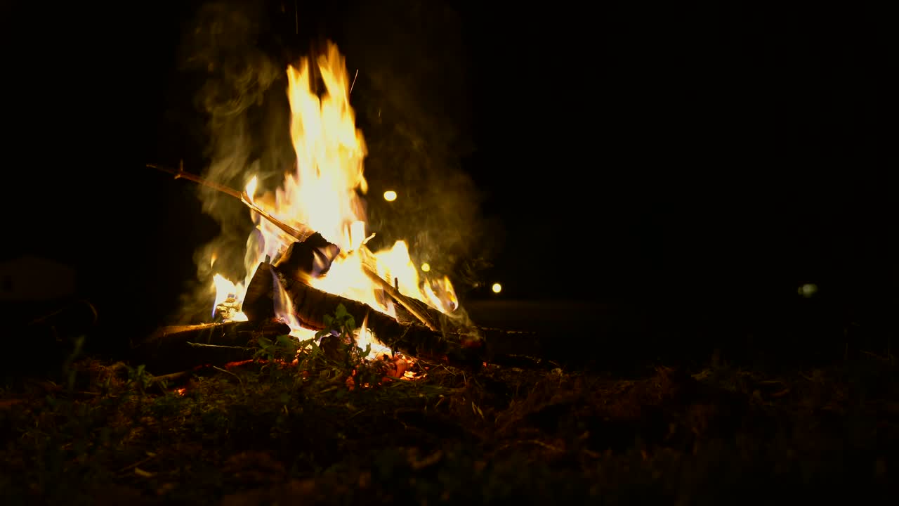 fotografía estática de un fuego de campamento por la noche mientras alguien agrega leña fresca al fuego
