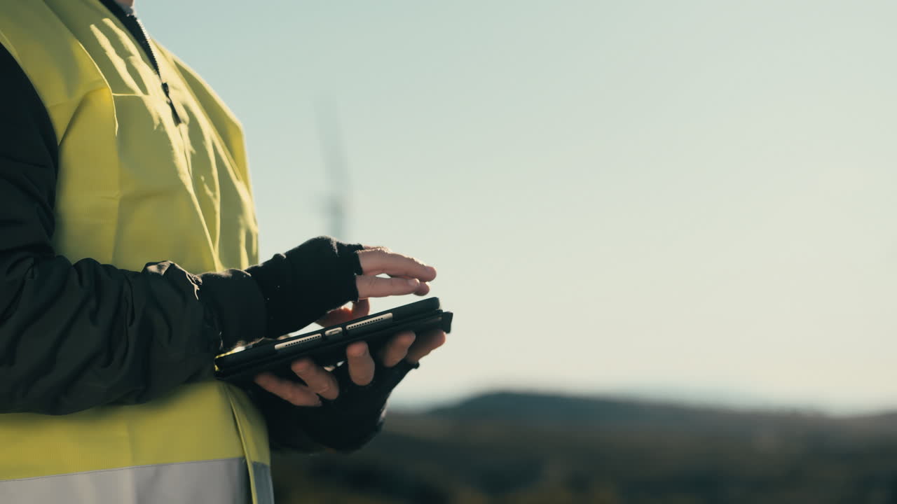 promoviendo un futuro más verde, un ingeniero usa un chaleco reflectante mientras usa software tecnológico en una tableta para auditar turbinas eólicas en un campo de generadores de energía renovable en un día soleado