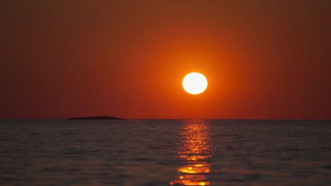 time lapse of the sun setting over the horizon at a scenic natural romantic calm water beach with small waves at the croatian mediterranean seaside as a big, orange ball. outdoors tourism vacation sunset cinemagraph seamless video loop im 4k uhd.