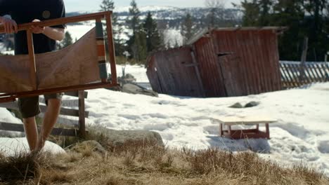 man setting up and sits down in a folding char in the sun in spring in norway with some snow left on the ground