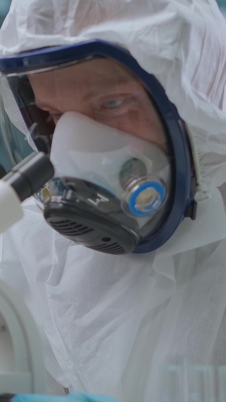 Scienziato in tuta protettiva che usa un microscopio in laboratorio
