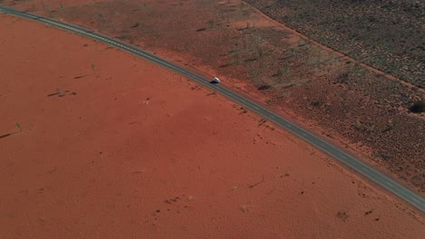 arid red desert with a white vehicle park in asphalt road during summertime in northern territory, australia