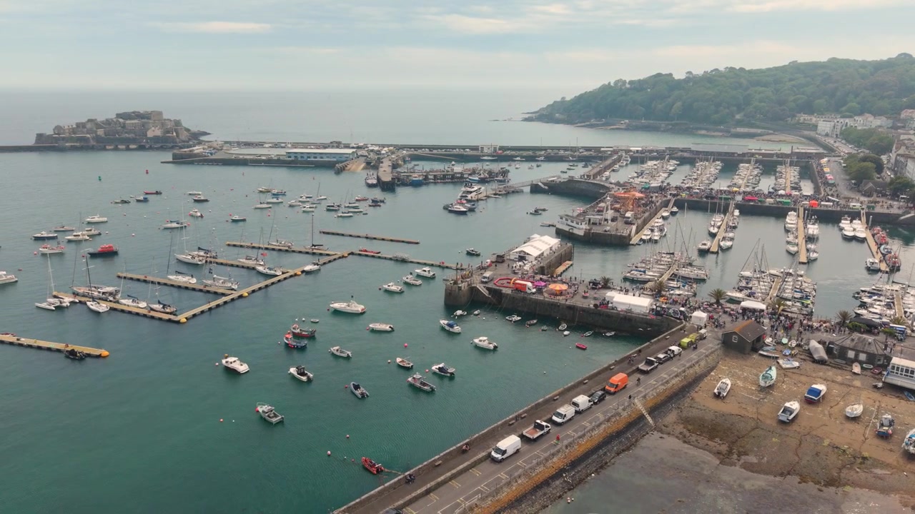 St Peter Port, Guernsey, Isole del Canale. Riprese aeree che si allontanano nel Giorno della Liberazione del porto di St Peter Port e del Castello Cornet, con luna park, bancarelle e tendoni allestiti intorno alla marina