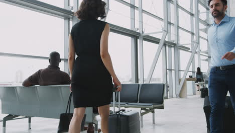 busy airport departure lounge with businesspeople wheeling luggage at taking seats