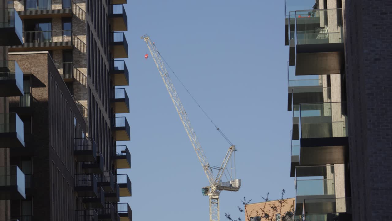 Enorme gru a torre da costruzione tra edifici residenziali che costruisce nuovi immobili a Londra, Regno Unito. Sfondo minimalista dello skyline urbano che rappresenta la crescita della città e la pianificazione futura