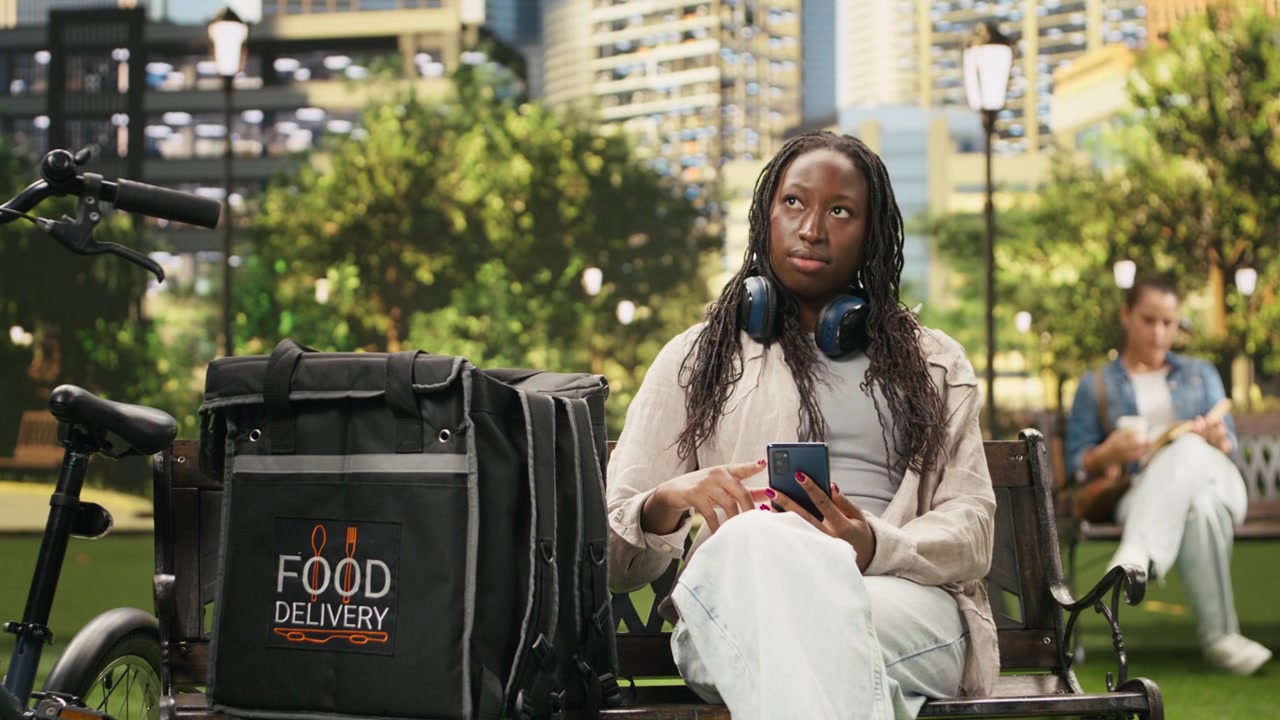 Food delivery courier resting and checking order request on smartphone