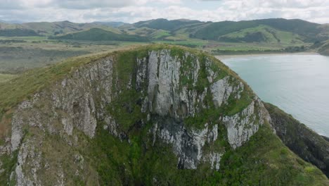 aerial drone flying over steep rocky cape landscape towards beautiful peaceful sandy beach in remote cannibal bay in the catlins, south island of new zealand aotearoa