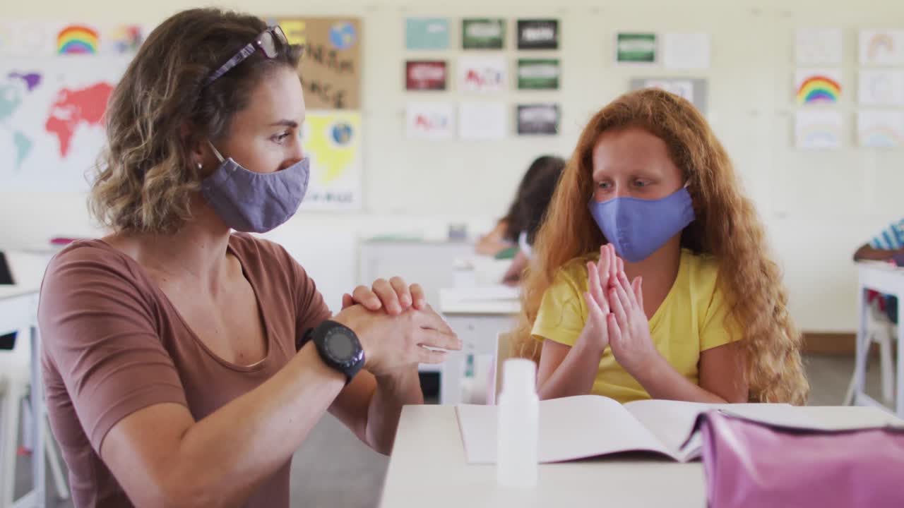 maestra y niña con máscaras faciales desinfectando sus manos en la escuela