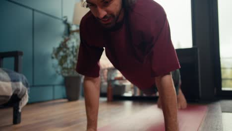 a happy brunette guy in a red t-shirt has done the push-up exercise at home, gets up on his feet and wipes his forehead. fitness at home