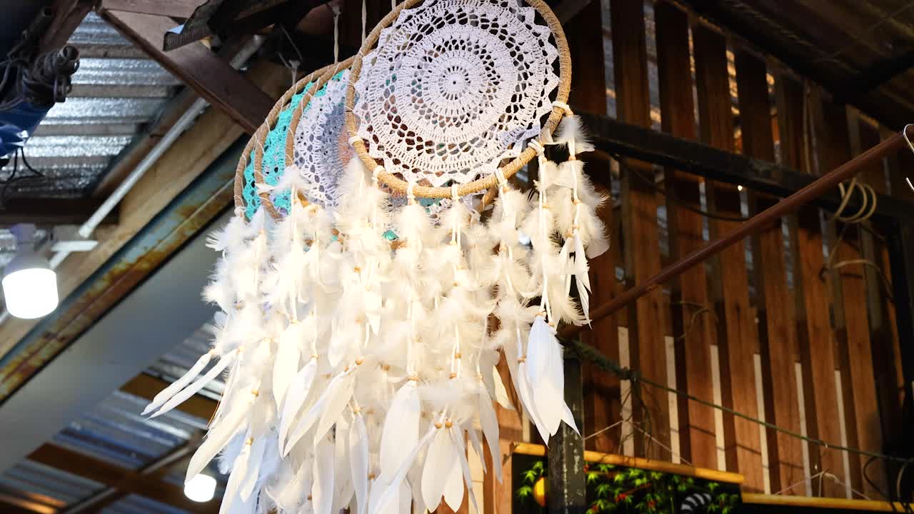 A dreamcatcher with feathers gently sways indoors, under warm lighting, creating a serene and calming atmosphere