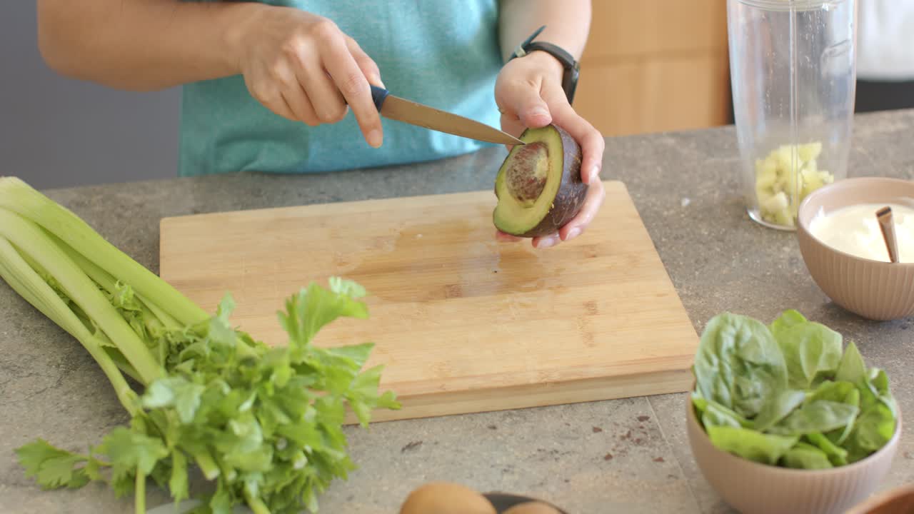 Avocado dimezzato che viene tagliato dopo essere stato posizionato sul tagliere, mentre delle mani rimuovono il nocciolo per l'insalata.