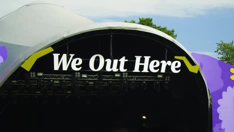 We-Out-Here-festival-sign-name-of-the-venue-hanged-on-the-main-stage-cover-with-massive-tent-and-scaffolding-that-holds-the-lighting-purple-yellow-funky-hippie-paintings-on-the-sides-summer-camp-music