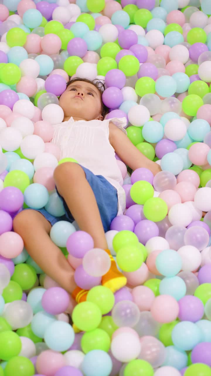Young child lies relaxed and happy amidst a vibrant sea of colorful pastel balls in an indoor play area