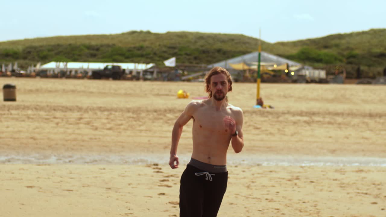 A Shirtless Man in Black Pants is Running on the Beach in Scheveningen, Netherlands - Wide Shot
