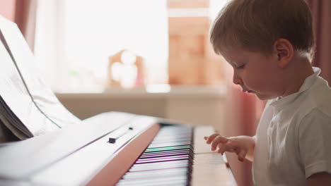 Concentrated-little-boy-plays-electrical-piano-in-light-room