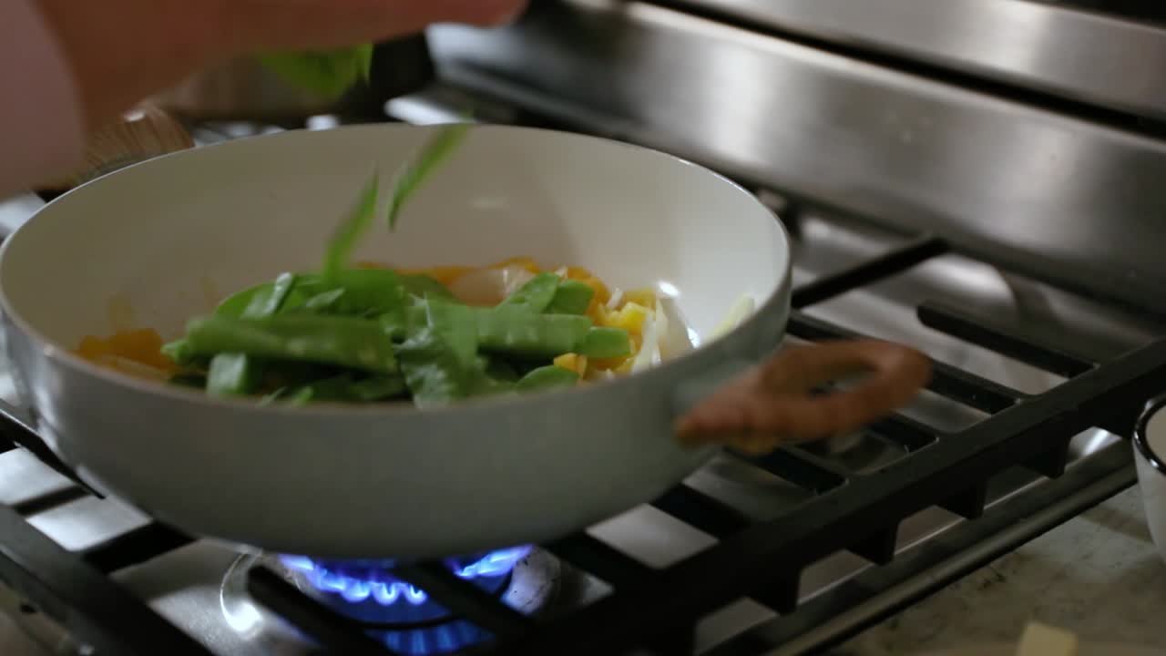mujer añadiendo guisantes de nieve a la sartén de cocinar verduras en cámara lenta