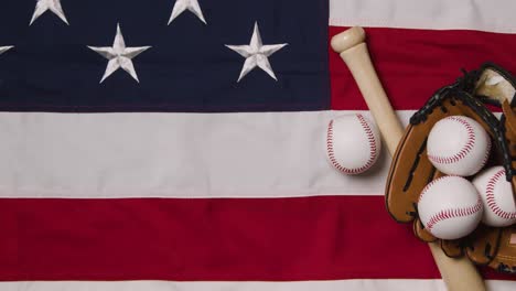 overhead baseball still life with bat and catchers mitt on american flag with ball rolling into frame