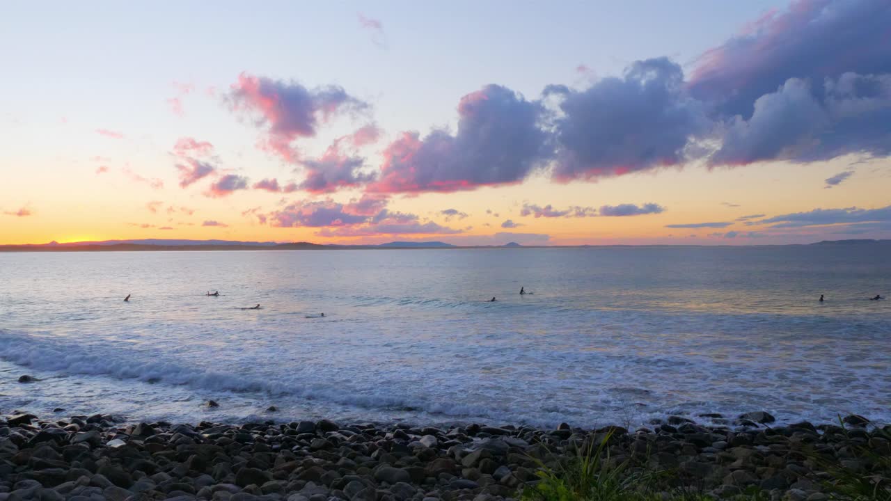 surfistas flotando en sus tablas de surf en la playa durante la puesta de sol en el parque nacional noosa en queensland, australia