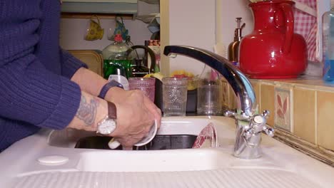 pots being washed by hand and put on to a white ceramic draining board to drain