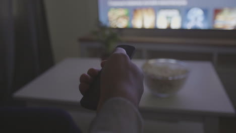 someone's hand with a remote control navigates through the tv menu for a programme or film to watch 1