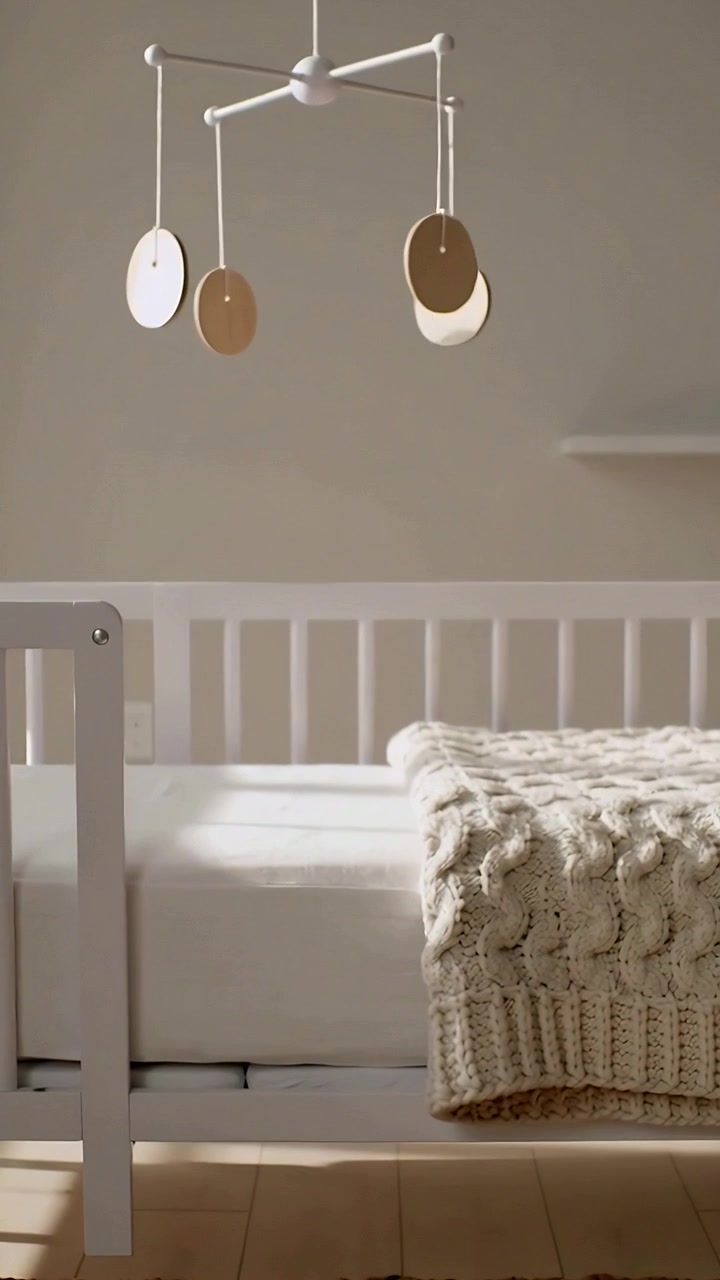 Vertical video: Rotating mobile above crib in nursery, sun shifting, casting shadows on blanket