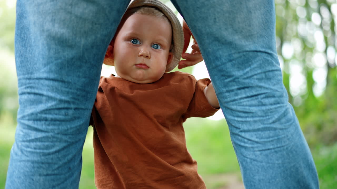 Beautiful Caucasian baby stands holding by the legs of his father. Little kid learning to stand and walk.