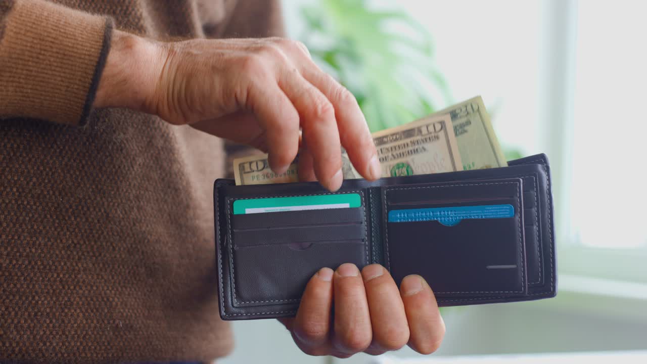 Primo piano delle mani di un uomo anziano che tira fuori banconote da un dollaro dal portafoglio.