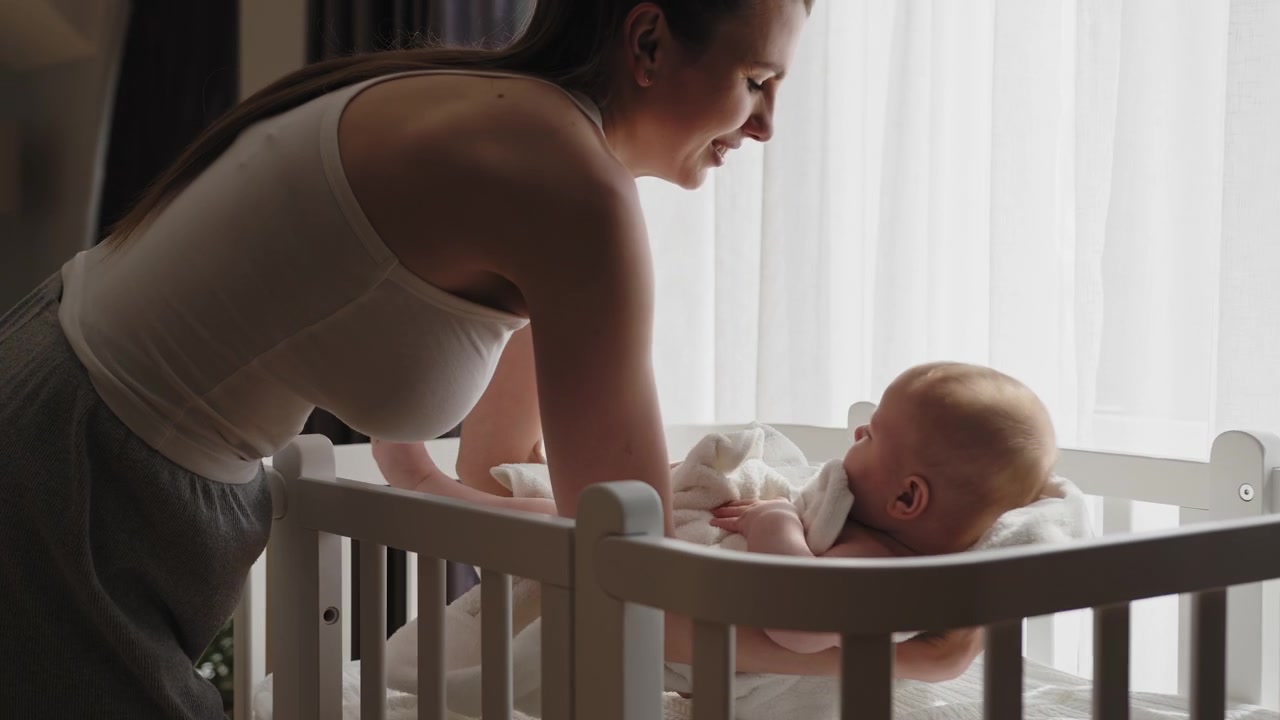 Une mère dépose délicatement son nouveau-né dans un berceau blanc, le préparant au sommeil avec une tendre attention