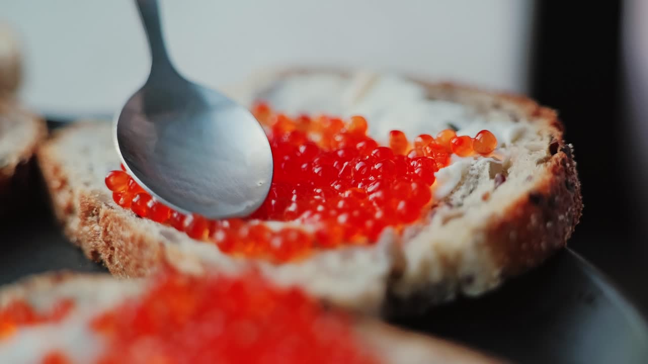 Extreme close up slow motion, red caviar spread on rustic buttered bread