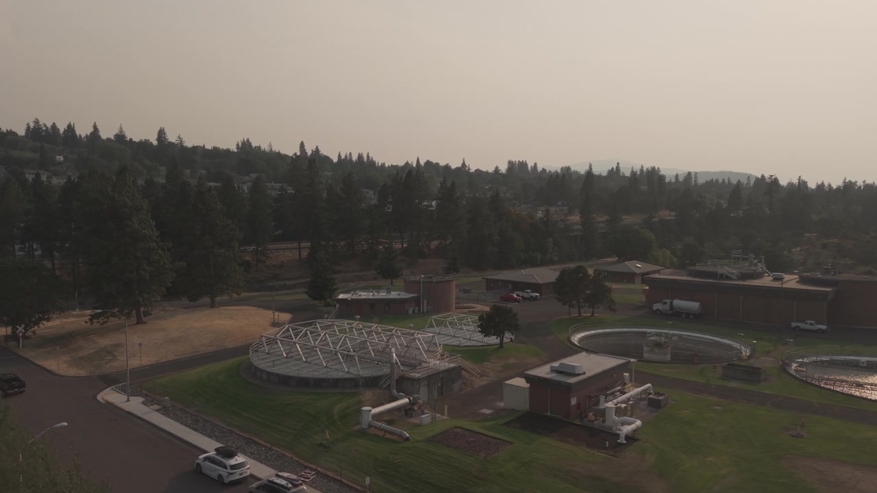 Hood River water treatment plant in Oregon surrounded by thick wildfire haze, with a drone pullback revealing the facility and surrounding landscape under reduced visibility.