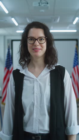 American-female-voter-or-polling-officer-speaks-on-camera,-calls-for-voting.-National-Elections-Day-in-the-United-States.-Voting-booths-in-the-background-at-polling-station.-Civic-duty-and-patriotism.