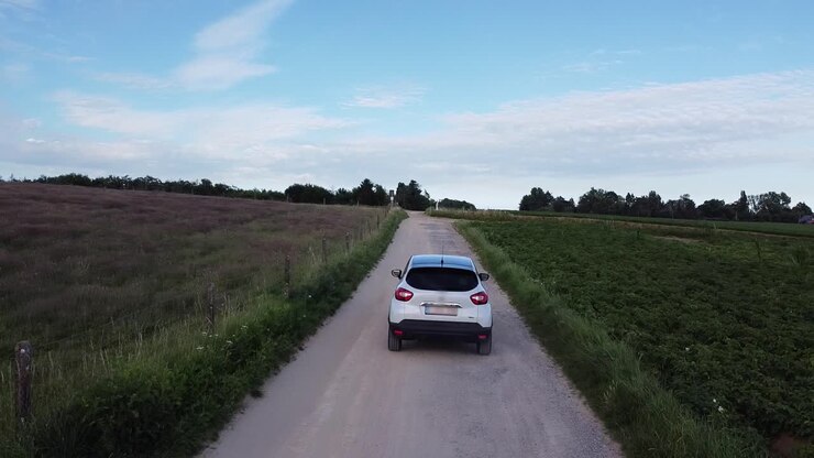 Auto bianca che procede lentamente su una strada sterrata tra i campi agricoli a Scherpenheuvel, Belgio.