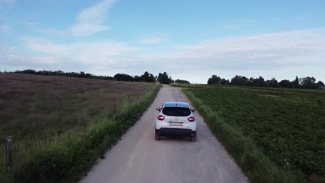 White-car-driving-slow-on-a-dirt-road-between-the-farm-fields-in-Scherpenheuvel,-Belgium