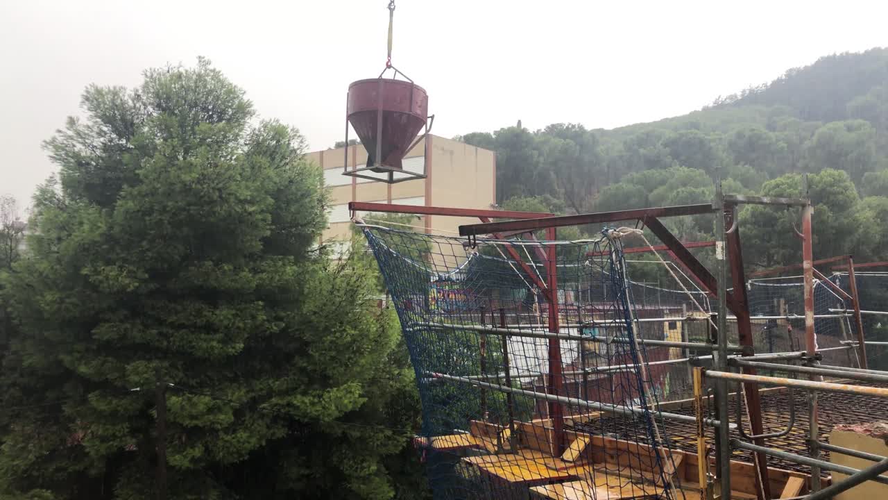 бетонный ковш, подвешенный краном в дождливый день на строительной площадке