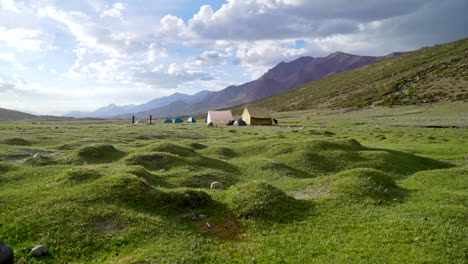 Low-angle-steady-shot-of-a-base-camp,-at-Nimaling,-and-tents-in-the-Himalayas,-as-two-hikers-walking-around