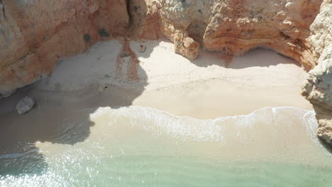 Beautiful-aerial-of-small-sand-beach-surrounded-by-tall-cliffs