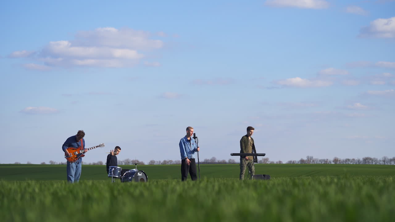 Four musicians performing their energetic music in the plantations. Young men create music, sing and move actively. Nature backdrop.